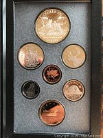 Front view inside coin set case showing all 7 coins including large silver dollar with explorers canoeing, and smaller denominations.