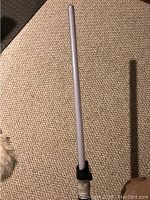 Red LED Star Wars light saber standing upright on carpet, showing the full lit blade.