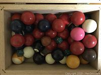 Top view of assorted smaller billiard and snooker balls along with pool chalk in a wooden box.