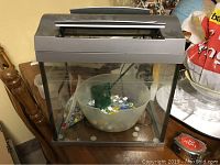 Full view of the assembled aquarium showing the glass tank with dark frame, internal bowl with marbles, and green feature inside.