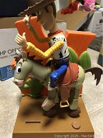 Front angle view of Woody on horse with orange 'Y' and cactus backdrop on tan base with coin slot.