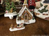 Detailed view of gingerbread house with sleigh figurine, showing intricate painted details and holiday motifs like gingerbread men and icing.