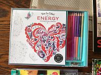 Adult colouring book 'Energy' with 12 coloured pencils and sharpener in a box, showing detailed cover art with butterfly and abstract design in red and purple.