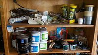 Shelf with assorted extension cords, timers, wasp traps, paint cans, and electrical boxes.