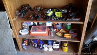 Shelf with assorted hand tools including pliers, screwdrivers, cordless drill, wrenches, and household chemicals such as WD-40 and spackling compounds.