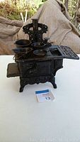 Front and side view of the black miniature cast iron stove with small cast iron pots and pans placed on top and sides.