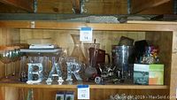 Shelf with various glassware and bar items including glasses, decanter, pitchers, metal ice bucket, and decorative letters spelling 'BAR'.
