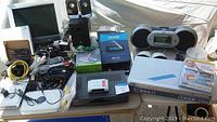 Wide view of all electronics including monitor, Sirius boombox, DVD/VCR combo, cables, and accessories on a table