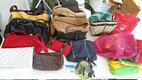 Full view of assorted bags and purses in the lot showing various sizes, colors, and types including several purses, a leather briefcase, and cloth bags.