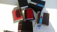 Top-down view showing multiple assorted blank journals and notebooks with different covers and bindings on a white background