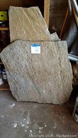 Photo of two large and one smaller stone slabs placed indoors on a concrete floor in front of shelves.