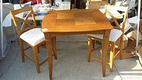 Full view of square wood game table with two chairs with white cushioned seats