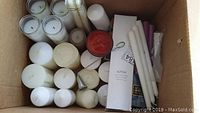 Box top-down showing various white pillar candles, taper candles, a red jar candle, and metal candle holder.