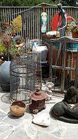 Wide shot showing multiple garden decorations including large metal birdcage, mermaid fountain, metal stands, and decorative statues.