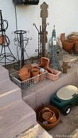Photo showing wrought iron plant stands, wooden plant stand, terra cotta pots in basket and stacked, metal Eiffel Tower, cat bird feeder, and wooden bird house