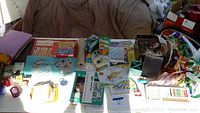 Wide table view of assorted arts and crafts supplies including papers, calligraphy books, stencils, chalk, ribbons, containers, and stamps.