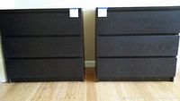Front view of two black Ikea dressers placed side by side on a wooden floor, each with three drawers and a minimalist handle design.