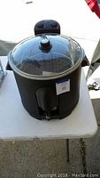 Black Masterbuilt electric turkey fryer with glass lid on a white table outdoors.