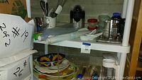 Shelf containing assorted kitchen items such as platters, bowls, cups, and utensils.