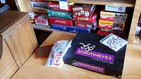 Photo showing multiple board games stacked including ScrutinEyes, card decks, and game pieces.