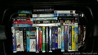 Top-down photo showing multiple VHS tapes in their cases arranged side by side with visible titles such as Independence Day, Swordfish, The Rock, He Got Game, Bad Boys, and various others.