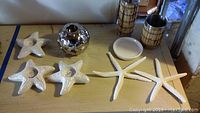 Photo showing four small white starfish tea light holders, one silver tea light globe holder, and two decorative large white starfish on table.