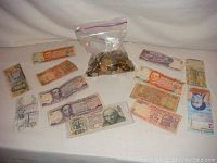 Assortment of foreign banknotes laid out flat next to a plastic bag containing more coins.