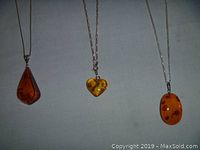 Three amber pendant necklaces laid flat showing pendants and chain details
