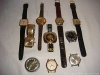 Front angled view of 10 vintage men's mechanical wristwatches laid out on flat surface showing various dial shapes and strap types