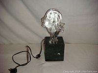 Front angle view of vintage glass lamp showing woman profile sculpture on marble base with power cord.