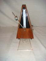 Front view of vintage German wooden metronome with bell, showing tempo scale and pendulum along with the transparent cover.