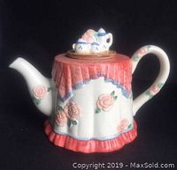 Front view of ceramic teapot with pink roses and red skirt design on black background