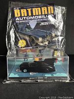 Front view of Batman Batmobile model in clear display case with Batman Automobilia magazine behind it showing the packaging and branding.