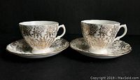Pair of Royal Vale tea cups and matching saucers with gold chintz floral pattern on white porcelain, shown side by side.