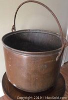 Front view of large copper pot with rusty handle and visible patina and dents.