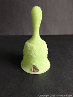 Front view of Fenton light green satin glass dinner bell with Daisy and Button pattern and Fenton label on base.