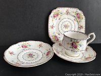 Front view of tea cup, two saucers, and one side plate showing floral petit point pattern and gold trim.