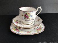 Tea cup stacked on saucer and side plate showing floral Petit Point pattern and scalloped gold-trimmed edges