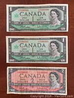 Front of two Canadian Centennial One Dollar bills with consecutive serial numbers and one Canadian Two Dollar bill, all featuring Queen Elizabeth II portraits.