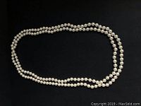 Full view of coiled 70-inch pearl necklace on black background