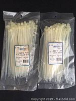 Two sealed packages of white nylon cable ties, each labeled with brand and specifications.