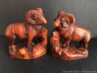 Front angled view of the pair of carved ram bookends showing detailed horns and rock base.