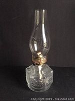 Full view of the 15-inch oil lamp showing clear chimney, brass burner, and square base with embossed scenes.