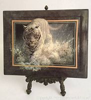 Front view of a limited edition ceramic collector tile depicting a white tiger splashing in water, mounted on a tall ornate brass display stand.
