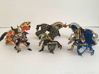 Front view of three medieval knights standing with three armored horses, showing colors and design details.