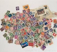 Wide view of hundreds of assorted postage stamps in various colors and sizes spread out, featuring diverse imagery of historical figures and scenes primarily from Canada and other countries.