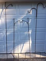 Photo showing four metal shepherd hooks against a garage door, two tall single hooks and two shorter double hooks with rust on bottom prongs
