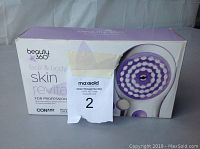 Box packaging front of Beauty 360 face and body skin revitalizer by Conair with purple and white brush head image.
