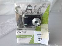 Front view of Vivitar Snap A Pic digital camera in original clear plastic packaging showing camera and branding.