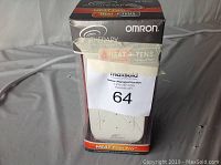 Front view of sealed Omron ElectroTherapy Heat + TENS device in original box showing product name and branding.